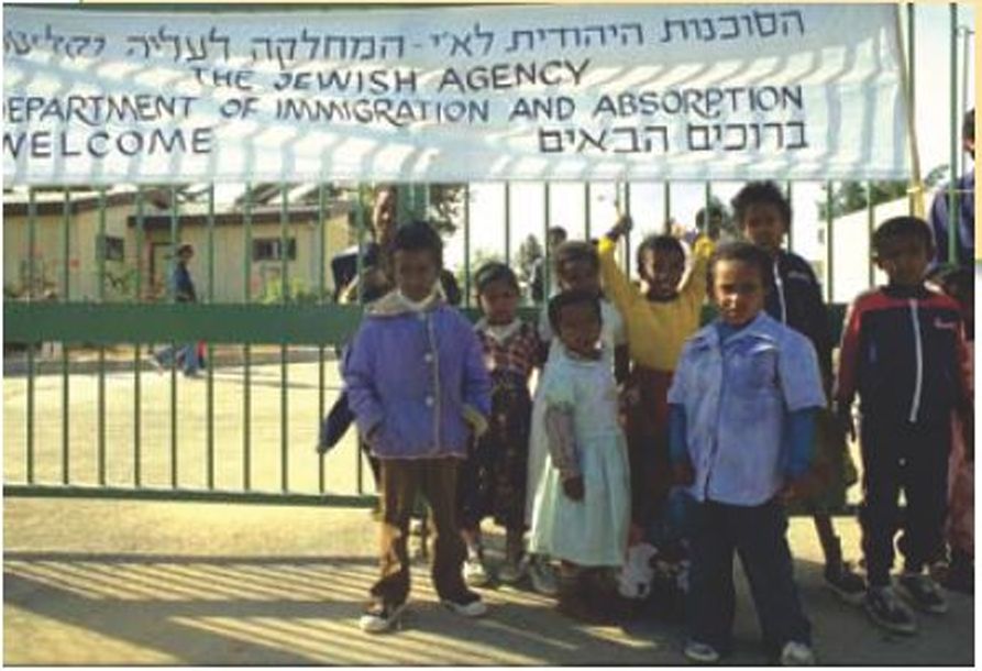עולים חדשים ליד שלט של המחלקה לעליה וקליטה של הסוכנות היהודית שכתוב עליו 